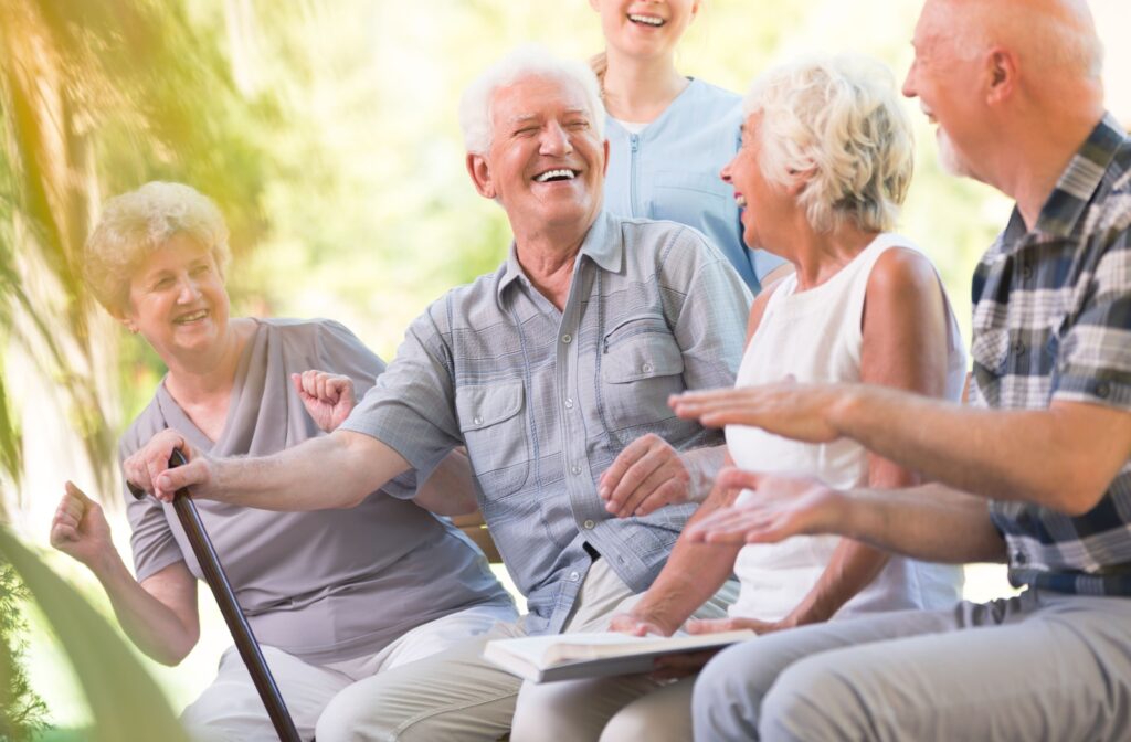 A group of older adults sitting together outdoors in sunshine, laughing, one holding an open book
